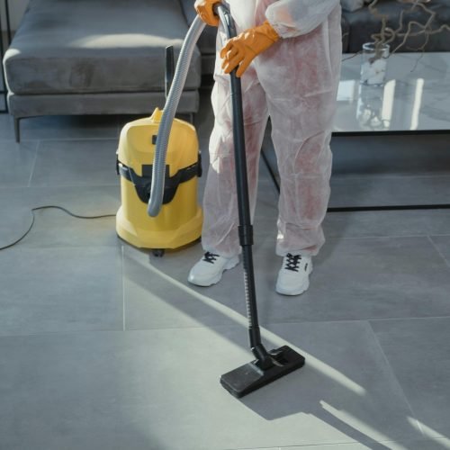 A professional cleaner in protective gear vacuuming the floor in a modern living room.
